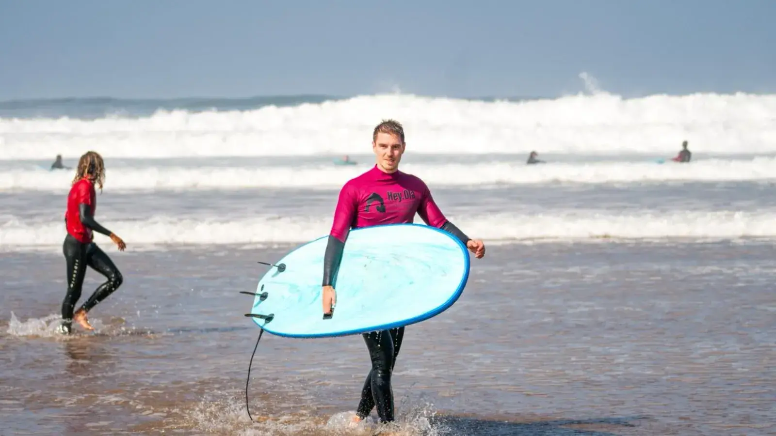Two beginner surfers walking out of the water at Mirleft, foam boards under their arms